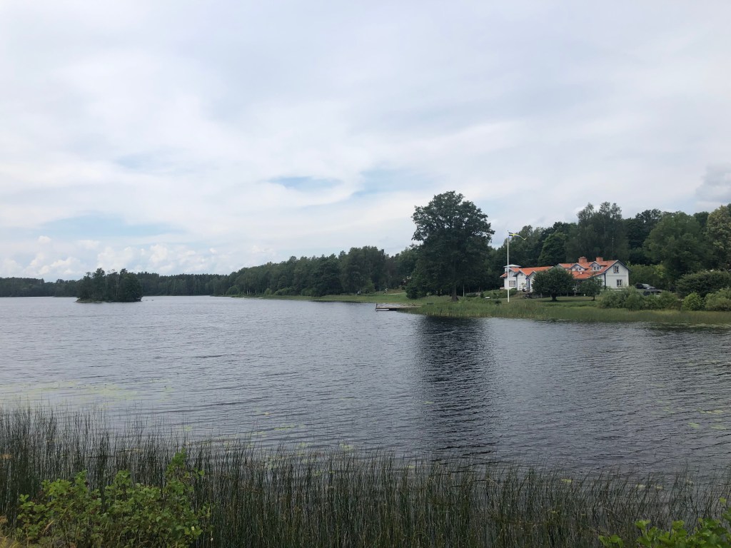 En herrgård vid en sjö och lätt molnigt på himlen.