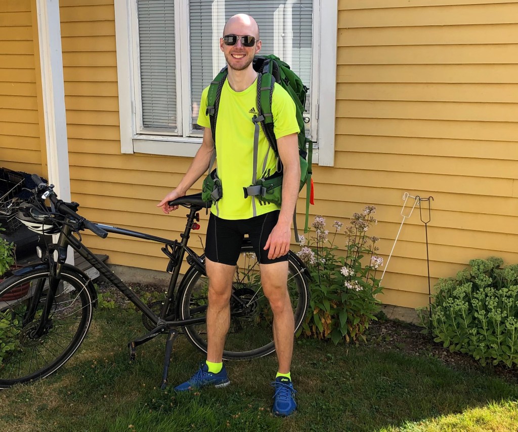 Jag med ryggsäck och solglasögon ståendes bredvid cykeln hemma i föräldrarnas trädgård.