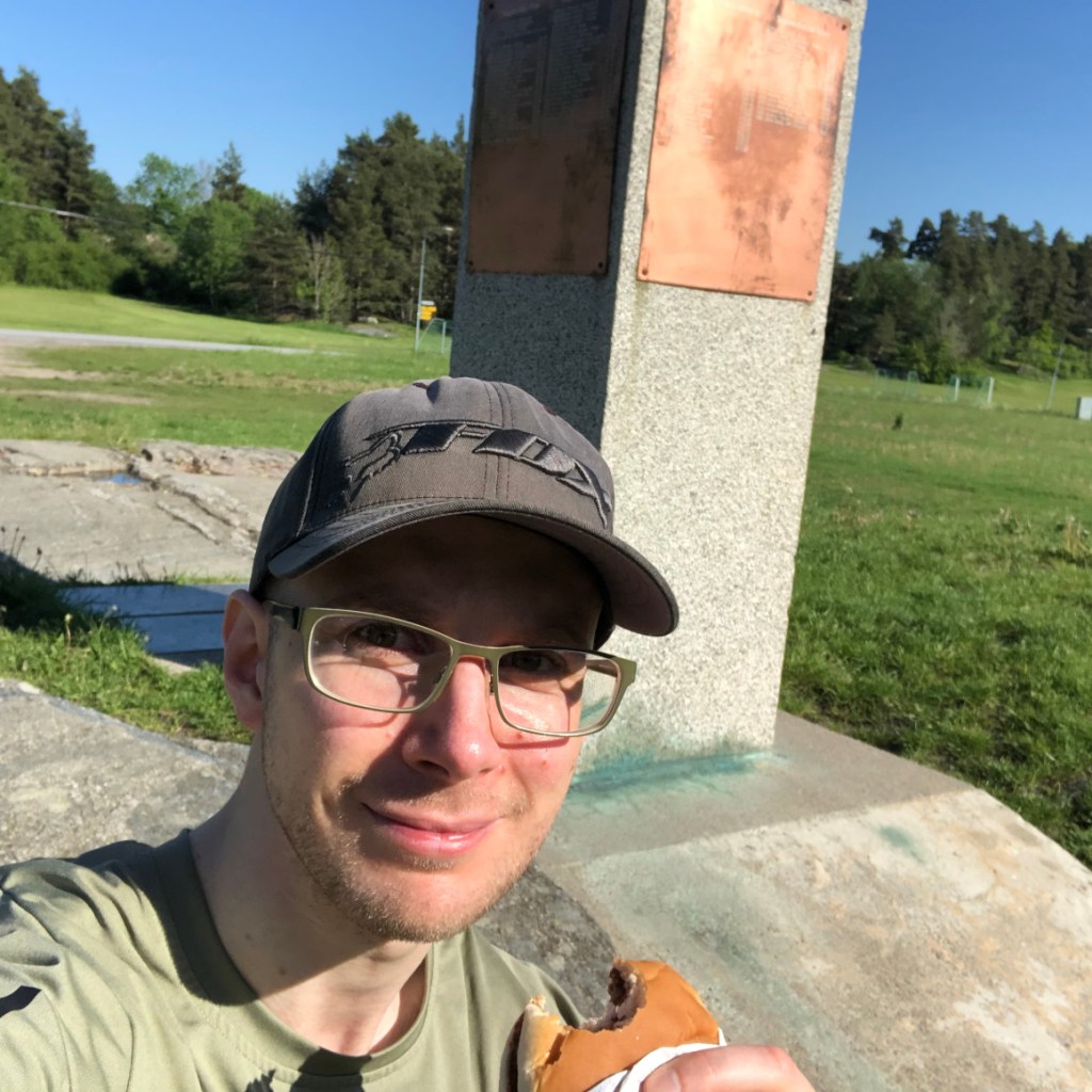 Selfie vid Löparmonumentet med en hamburgare i handen.
