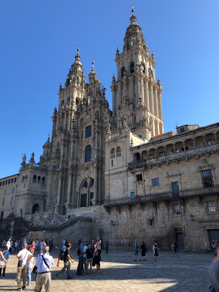 Katedralen i Santiago de Compostela. Pilgrimsvandrare och turister i förgrunden. Klarblå himmel.